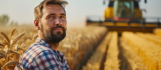 Contented farmer in a field, combine harvester operator approaching bountiful wheat harvest, agronomist in plaid shirt gazing at camera on a farm
