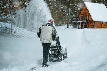 Man removes snow with a snowblower rear view. working with a gasoline snow blower after the severe winter storm in the city. Clearing the area from snowfall.