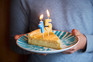 A piece of cake with the numbers 15 in the hands of a teenager. The fifteenth birthday. A cake on a...