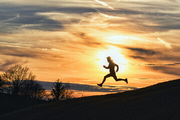 Sporty man runs down hill in silhouette