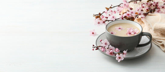 Spring twigs with flowers with a cup of hot drink, on a light wooden background. - obrazy, fototapety, plakaty