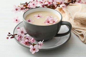 Spring twigs with flowers with a cup of hot drink, on a light wooden background.