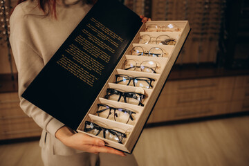 Close up of woman taking eyeglasses from rack. Female choosing stylish prescription glasses on eyewear display stand in optical store. Vision health, blindness concept. Selective focus