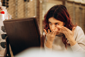 Beautiful young woman trying to put contact lenses for the first time. Behind her male optician
