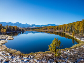 Breathtaking aerial shot capturing a tranquil mountain lake surrounded by autumn colors and snow dust in Altai.