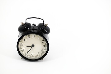 A black alarm clock with two bells on top, chrome handle, and legs, set against a white background. Timeless design meets functionality in this sleek, monochromatic timepiece..