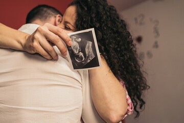 Pregnant Woman Embracing Future Baby’s Father Holding Printed Ultrasound. Young pregnant girl...