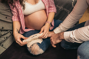 Unrecognizable pregnant woman at home wrapping baby bodysuit on floor while man is observing....