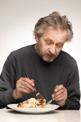 Older man eating spaghetti with minced meat, tomatoes and cheese