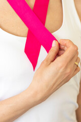 Shot of the woman in the white top against the white wall, with pink ribbon on her neck as a symbol of breast cancer awareness. Concept