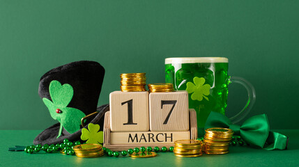 March 17th scene: side view of table with timber calendar, lager glass, clover leaves, gold pieces, leprechaun top hat, bow tie, strands of beads on a green canvas - Powered by Adobe