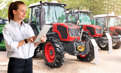 Female sales representative showcasing agricultural tractors with digital tablet. Businesswoman in...