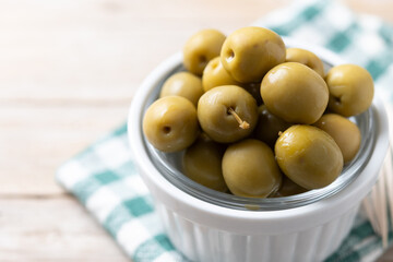 Green olives in a bowl on wooden table. Close up