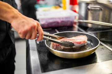 Professional chef cooking pork meat in frying pan on stove in restaurant kitchen