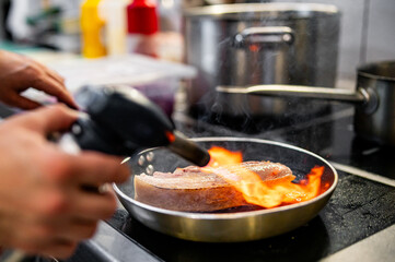 Professional chef cooking pork meat in frying pan on stove in restaurant kitchen