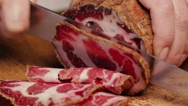 Chef slices a large piece of cured meat into thin slices. Italian coppa, prosciutto, ham