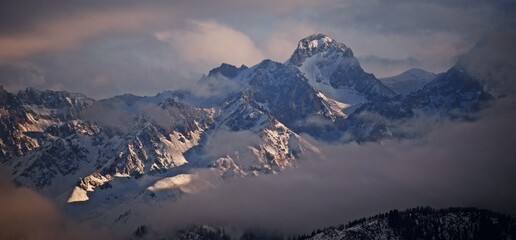 Beautiful view to the snowy winter mountain peaks cloudy sky and golden hour sunlight