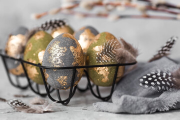 Stylish beautiful Easter eggs with golden enamel, willow branches and feathers on a gray...