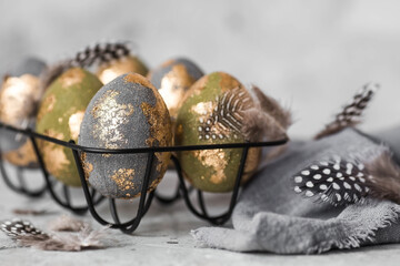 Stylish beautiful Easter eggs with golden enamel and feathers on a gray background. The concept of happy Easter 2024.