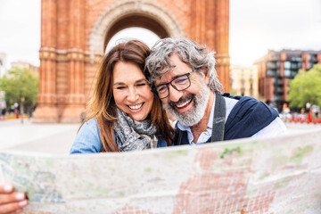 Married couple visiting Triumphal Arch in Barcelona, Catalonia, Spain - Two senior tourists holding city map walking in the street - European landmark