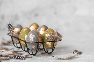 Stylish beautiful Easter eggs with golden enamel and feathers on a gray background. The concept of happy Easter 2024.