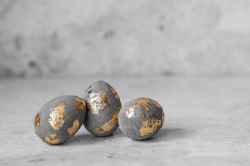 Stylish beautiful grey Easter eggs with golden potali coating on a grey background. The concept of happy Easter 2024.