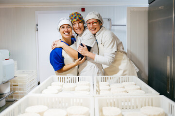 Happy female workers embracing near cheese at factory