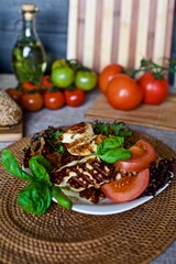 Healthy homemade fried halloumi cheese with red tomatoes and basil laying on the white plate in the kitchen 