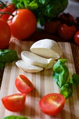 Flat lay of healthy homemade mozzarella cheese, red tomatoes and basil laying on the wooden cutting board