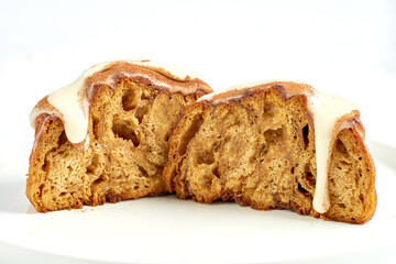 A cinnamon roll is poured with custard and sprinkled with cinnamon on a white background.