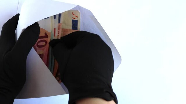 Billetes de euro dentro de un sobre blanco y unas manos con unos guantes negros se lo llevan. concepto de delito, robar, defraudar, impuestos.