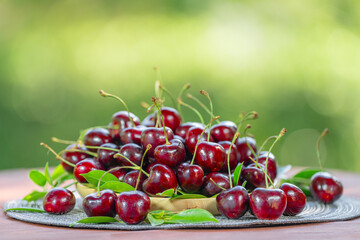 Red Cherry in basket on blurred greenery background.