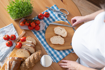 A pregnant young woman spreads curd cheese on slices of bread. View from above