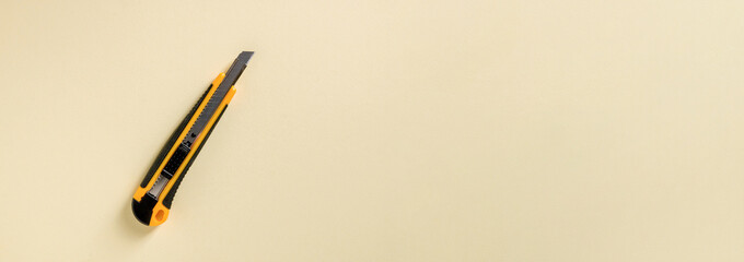 Utility knife with yellow and black handle on a yellow background