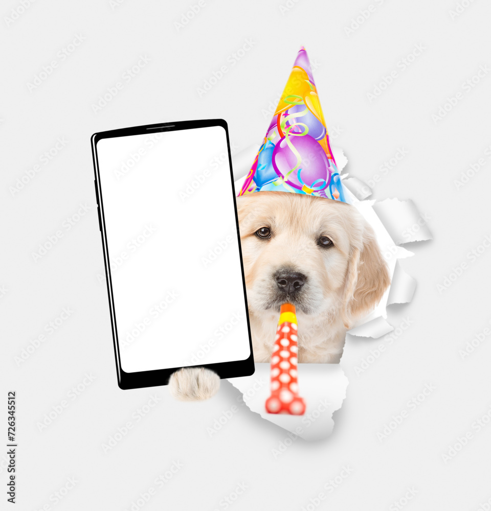 Poster golden retriever puppy wearing party cap blows in party horn and shows big smartphone with white bla
