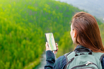 Young woman uses smartphone at sunny mountains and using travel app or map during her hike. Empty space for text - obrazy, fototapety, plakaty