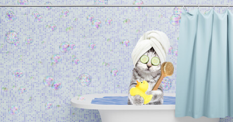 Cute kitten with towel on it head, pieces of cucumber on it eyes and with cream on it face takes the bath at home with rubber duck and shower brush