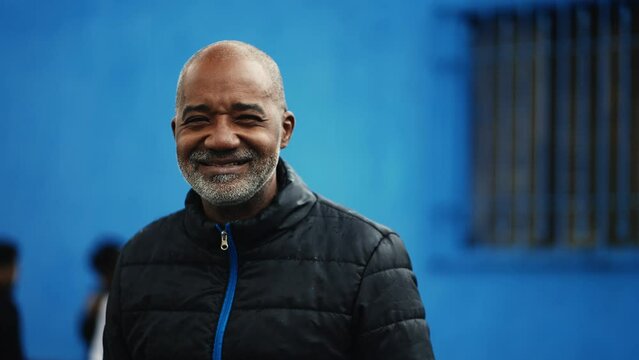 One happy middle-aged South American black man of African descent smiling at camera while standing outside in urban environment, Gray-haired bald person in 50s portrait