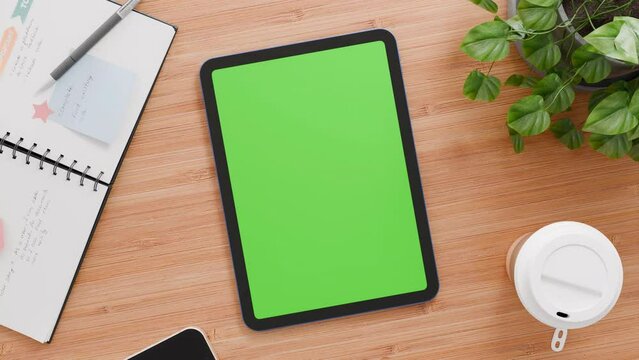 tablet with blank green screen, slow zooming animation, top view, office desk with accessories