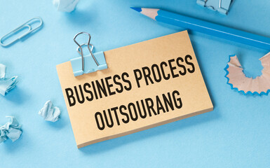 Business process outsourcing concept on sticky note with paper clips and pencil on blue background