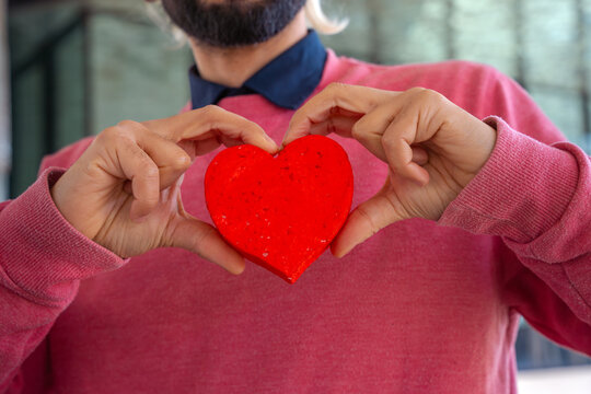  Portrait of a smiling young man holding a heart on Valentine's Day outdoors.