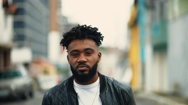 One young black guy walking forward towards camera in urban environment. Portrait face of an African American person looking at camera with serious gaze