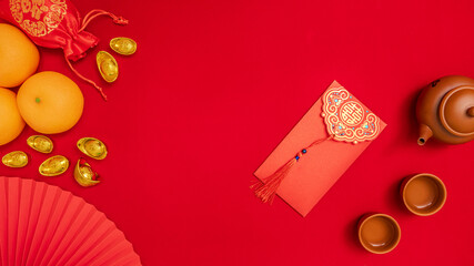 Chinese Lunar New Year background, red theme. flat lay silk bag with ancient gold bar, orange, paper hand fan, teapot, tea cup, red envelope, ang pow for give away money on Chinese new year celebrate