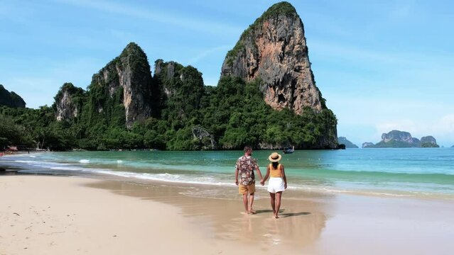 Railay Beach Krabi Thailand a tropical beach with a turqouse colored ocean, a couple of men and women walking on the beach. European men and Asian woman walking on the beach