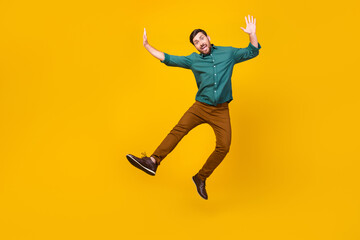 Fototapeta na wymiar Full length photo of childish playful man dressed dotted shirt flying hands up fooling around isolated on vibrant yellow color background