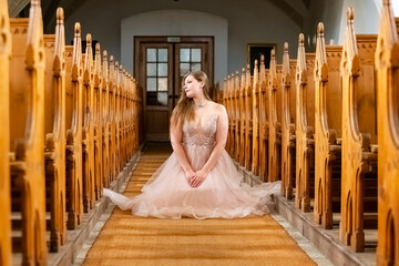 young woman in a pink dress squats in a church