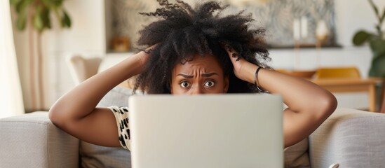 Upset black woman feeling frustrated and panicked by laptop issues on the sofa at home.