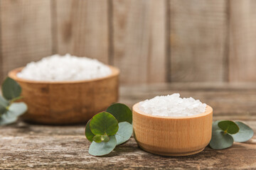 Cosmetic sea salt with aroma and eucalyptus extract on a textured wooden background with branches of fresh aromatic eucalyptus.Spa concept. Bath salt. Close-up. Space for text.Body care.copy space