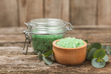 Cosmetic sea salt with aroma and eucalyptus extract on a textured wooden background with branches of fresh aromatic eucalyptus.Spa concept. Bath salt. Close-up. Space for text.Body care.copy space