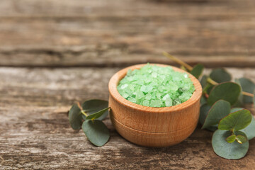 Cosmetic sea salt with aroma and eucalyptus extract on a textured wooden background with branches of fresh aromatic eucalyptus.Spa concept. Bath salt. Close-up. Space for text.Body care.copy space